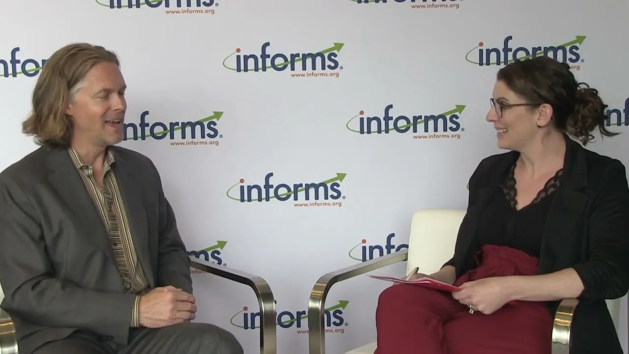 Matt Brady and Kara Tucker seated in front of an INFORMS backdrop